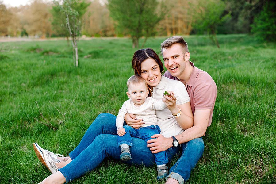 Get a Quote - Young Family Sits In the Grass on a Summer Day, Smiling For the Camera