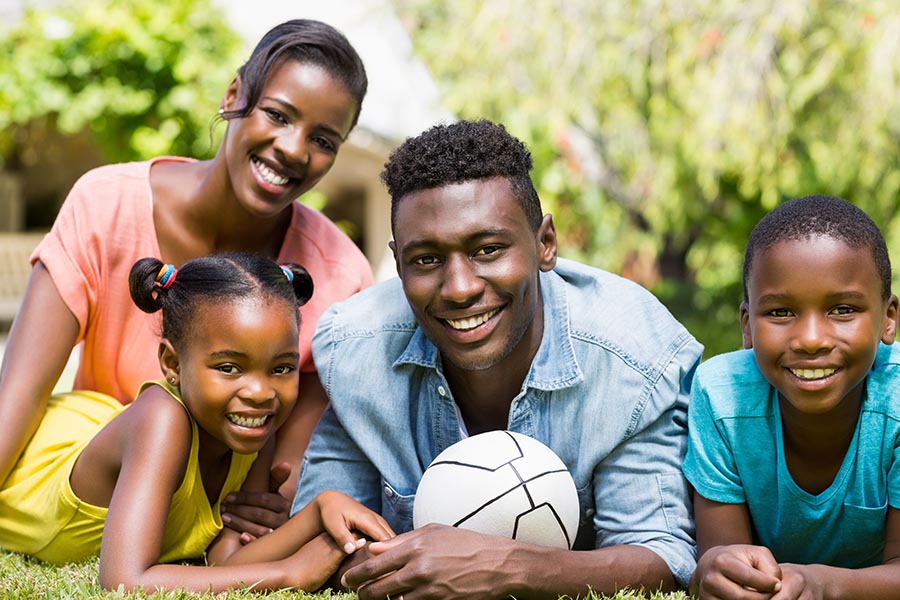 Personal Insurance - Family of Four Lays In the Grass With a Soccer Ball on a Sunny Day, All Wearing Brightly Colored Shirts