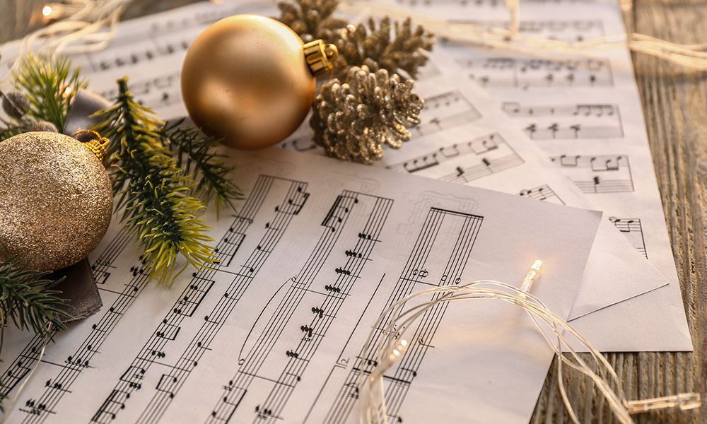 Blog - Golden Ordainments, String Lights, and Pine Tree Sticks Sitting on Top of Sheets of Music on a Wooden Table